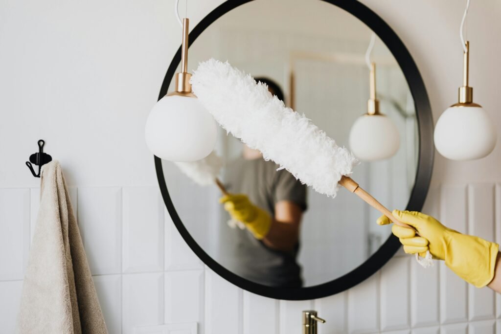 pexels-photo-4239031-4239031 A person cleaning an elegant bathroom mirror with a fluffy duster and yellow gloves.