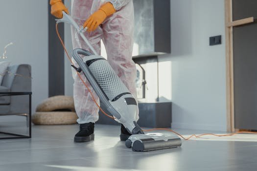 pexels-photo-6195955-6195955 A person in protective attire cleaning a modern room with a vacuum. Bright and tidy atmosphere.